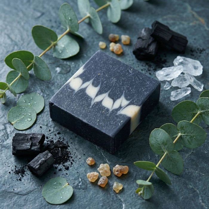 Black soap bar with white swirls on a dark surface with eucalyptus leaves and crystals.