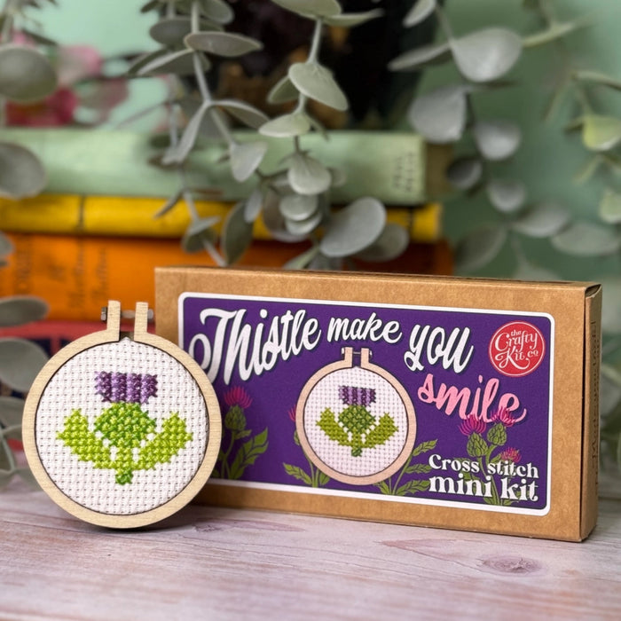 Cross-stitch mini kit with a completed design and packaging on a wooden surface.
