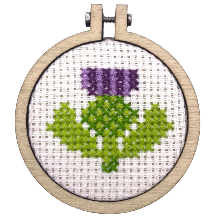 Embroidery hoop with a purple flower and green leaves on white fabric