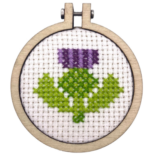 Embroidery hoop with a purple flower and green leaves on white fabric