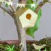 Gold birdhouse ornament hanging from a branch with green leaves and small decorative flags.