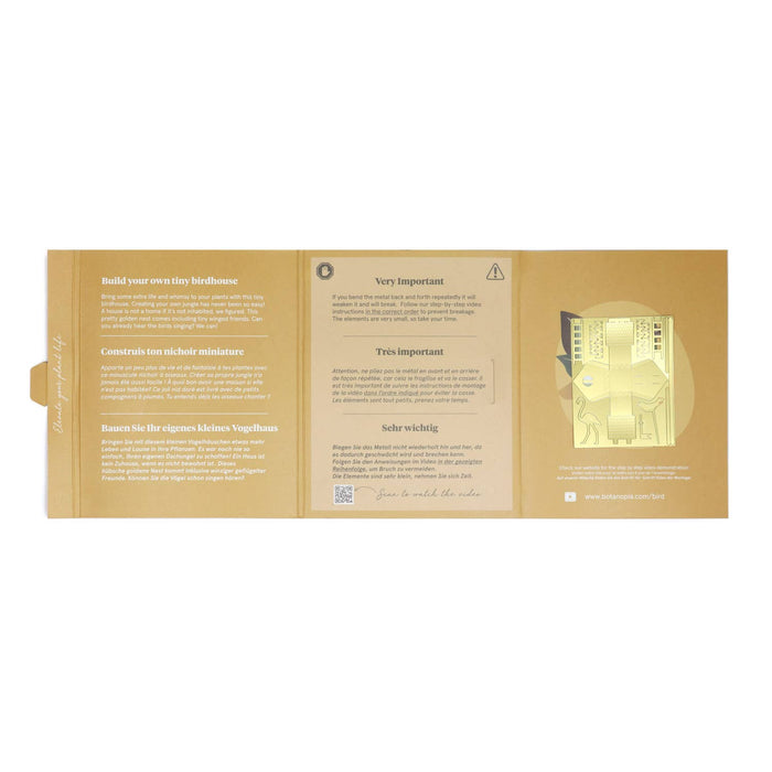A gold-colored instruction booklet or card set for building a tiny house, featuring German text instructions and a small illustration of a house on the right side.