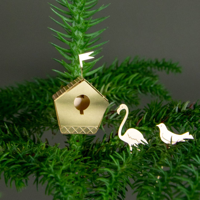 Gold birdhouse ornament with two white birds on a green branch against a dark background