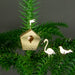 Gold birdhouse ornament with two white birds on a green branch against a dark background