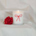 Candle with a red bow design and a red flower on a white blanket