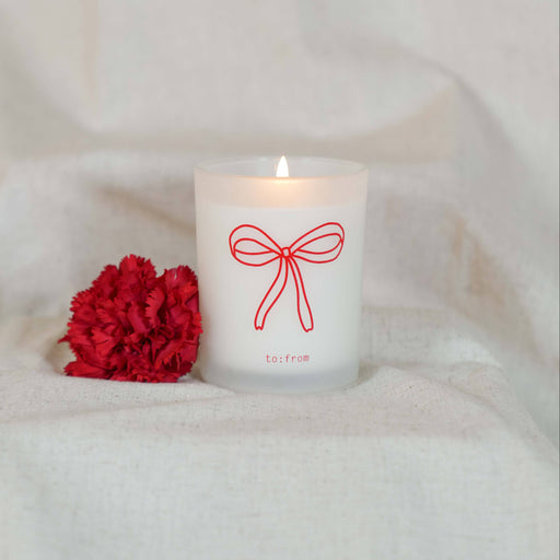 Candle with a red bow design and a red flower on a white blanket