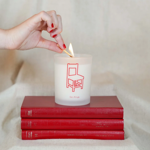Hand lighting a candle with a chair design on it, placed on two red books.
