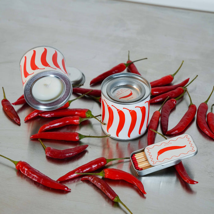 Two small metal cans with red and white striped lids, surrounded by red chili peppers on a light gray surface.
