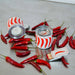 Two small metal cans with red and white striped lids, surrounded by red chili peppers on a light gray surface.