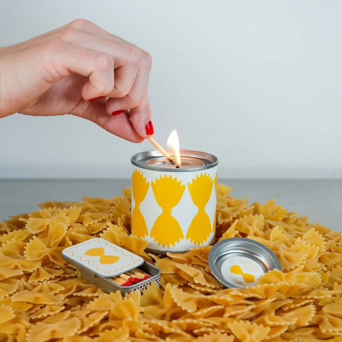 Candle being lit with a match on a bed of pasta, with a hand holding the match.
