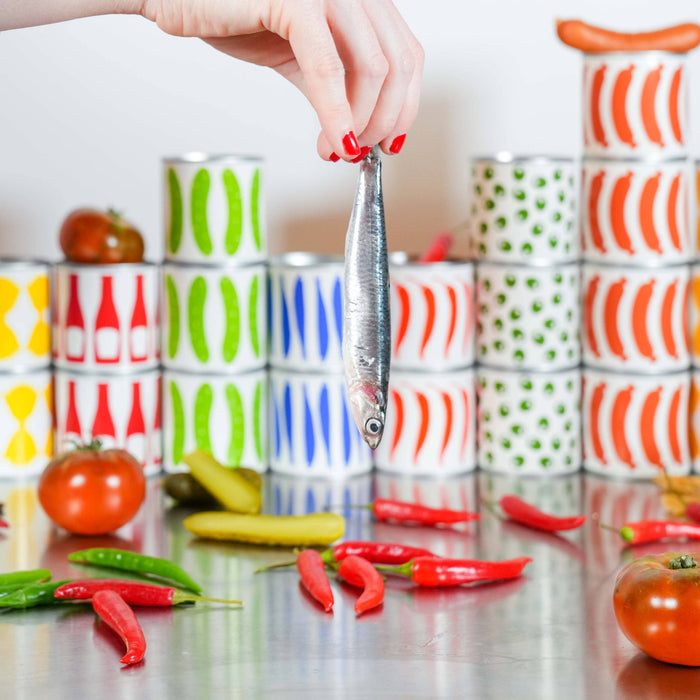 Colorful stacked canisters on a kitchen counter with a person's hand reaching out holding a sardine.