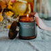 turf fire candle. Lit candle in brown glass jar. jar has a green label with white text