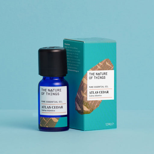 Atlas cedar essential oil blue bottle to left of a turquoise product box against a blue background