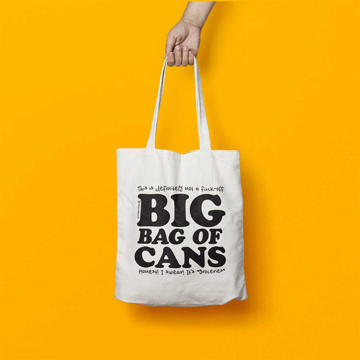 Tote bag being held by a hand at the top of the image. Tote is white with Big Bag of Cans in large black text on the front with smaller text above and below, bag in is front of a yellow backdrop 
