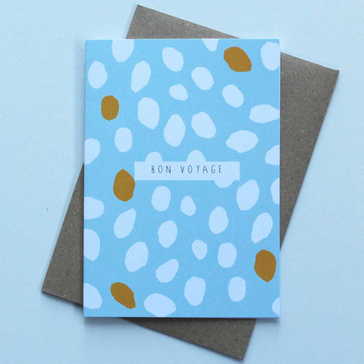 light blue greeting card in front of brown envelope with yellow and white spots and Bon Voyage in black text in centre