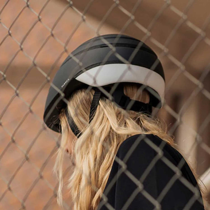 woman with blond hair seen from the back wearing a black helmet with white stripe
