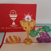 red pop up card with On Your Communion and Chalice image on front both in white, behind  open pop up card showing 3d paper chalice, purple grapes an d loaf of bread