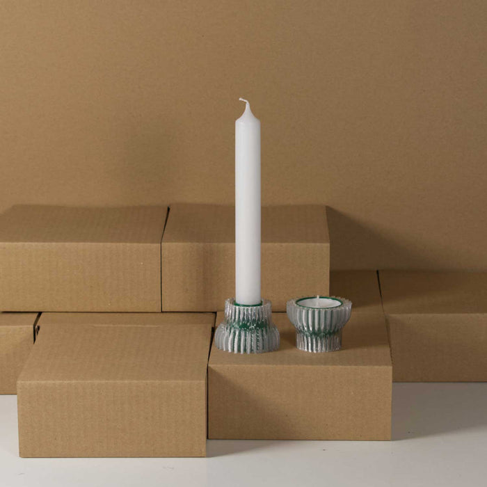 two green tinted ridged candle holders, one with a white tall dinner candle the other with a round tealight. They sit on cardboard boxes