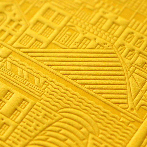 close up of yellow debossed image of a city bridge with buildings and water