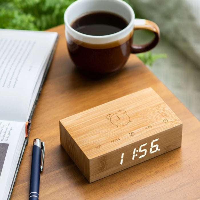 wooden flip clock showing the time on a digital face on a wooden table with a mug, book and pen in the background