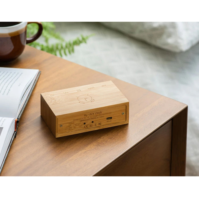 back of wooden flip clock showing the charging port on a digital face on a wooden table with a mug, book and pen in the background