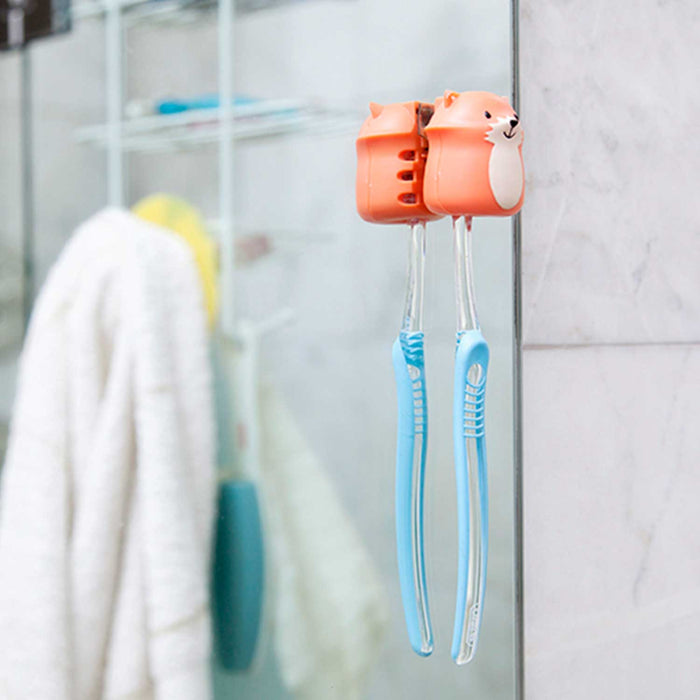 orange and white fox shaped toothbrush holder stuck to a mirror holding a blue toothbrush with white towel and grey tiled wall in background