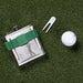 STAINLESS STEEL FLASK WITH TWO GOLF TEES ATTACHED WITH GREEN STRAP, LAYING ON GRASS WITH A STEEL PIN MARKER AND GOLF BALL TO THE RIGHT