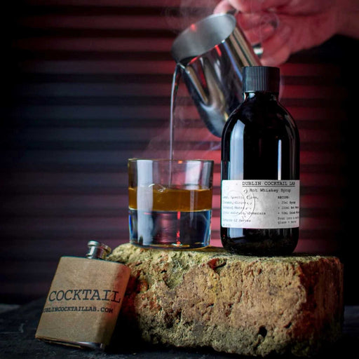 hand pouring hot liquid into a whiskey glass sitting on a brick with a dark glass bottle to the right 