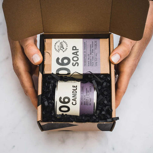 hands holding an open cardboard box with a bar of soap and candle tin inside both with with and purple packaging