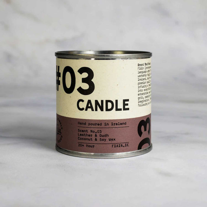 round metal tin with white and brown label with 03 candle in black text, against a grey backdrop