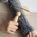 hand holding a wooden and metal lint remover over a grey knitted woollen sleeve