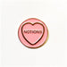pink circular enamels pin with gold circumference, a gold heart and text in the heart that reads 'notions' in front of a white background