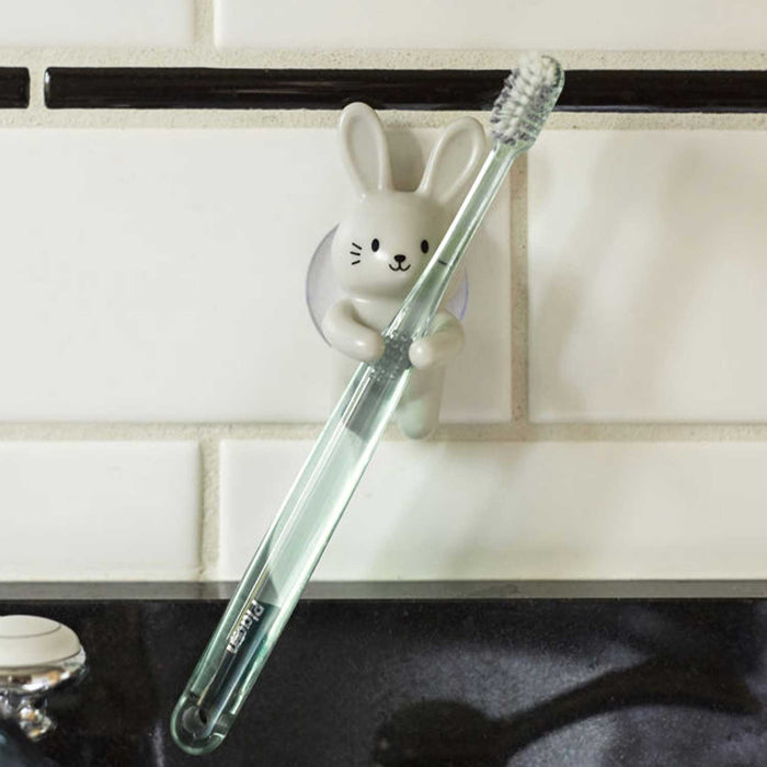 White rabbit toothbrush holder stuck to a tiled wall holding a toothbrush