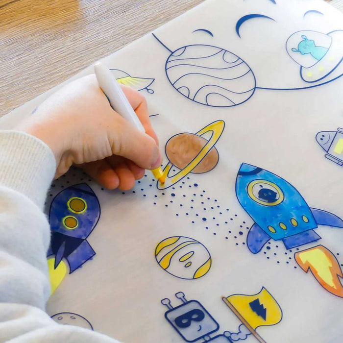 child's hand holding a yellow marker, colouring in a planet on a printed table mat.