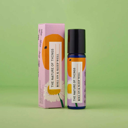 Roll On & Sleep Well essential oils blue bottle with black lid to right of pink and orange product box in front of a green backdrop