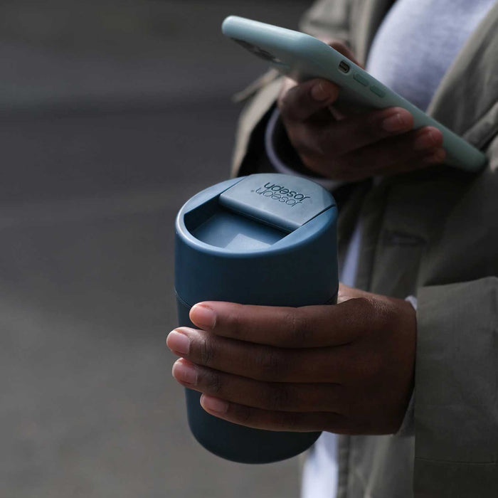 close up of hand holding a teal flask with lid  and phone in other hand
