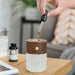 a hand dropping essential oil into the smart diffuser lamp on a wooden table