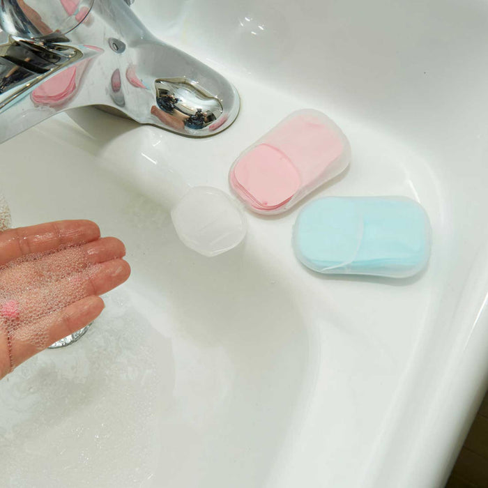 a green and a pink soap container on a white sink with chrome tap to the left in and upturned hand with soap bubbles