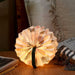 circular accordion shaped light with patterned paper on a wooden table n front of cushions and beside magazines