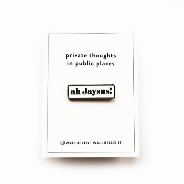 white backing card with black text and white enamel pin with 'ah jaysus!' in black on a white background