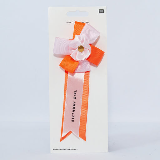 pink and orange rosette with birthday girl written on it on an off white background