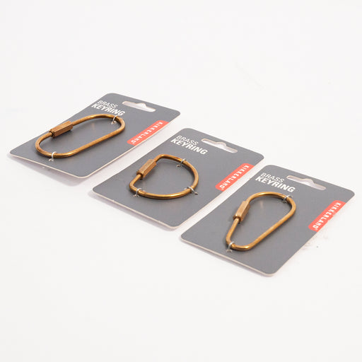 three different shaped brass keyrings on grey backing cards sitting on a white surface