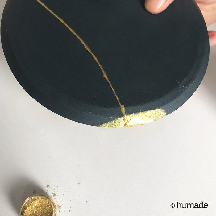 black plate being repaired with gold dust and kintsugi