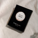 A black rectangular product box with a circular white and beige label reading 'flavours of Merlot' and smaller text 'The Real Wine Gum Wine Design,' photographed on a light fabric surface.