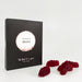 A black rectangular product box with a circular white and beige label reading 'flavours of Merlot' and smaller text 'The Real Wine Gum Wine Design,' photographed on a light fabric surface next to some red gummies.