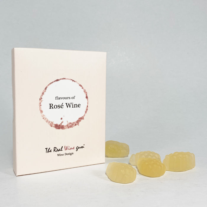 A cream rectangular product box with a circular white and sand coloured label reading 'flavours of Rose Wine' and smaller text photographed on a light fabric surface next to yellow gummies.