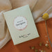 A light green rectangular product box with a circular white and sand coloured label reading 'flavours of Sauvignon' and smaller text 'The Real Wine Gum Wine Design,' photographed against beige fabric and an orange surface.