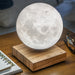 smart moon lamp above wooden base on a wooden table beside glasses and a notebook