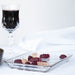 A glass dish of assorted gummies with a glass of red wine in the background against a white backdrop.