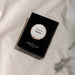 A black rectangular product box with a circular white and beige label reading 'flavours of Merlot' and smaller text 'The Real Wine Gum Wine Design,' photographed on a light fabric surface.